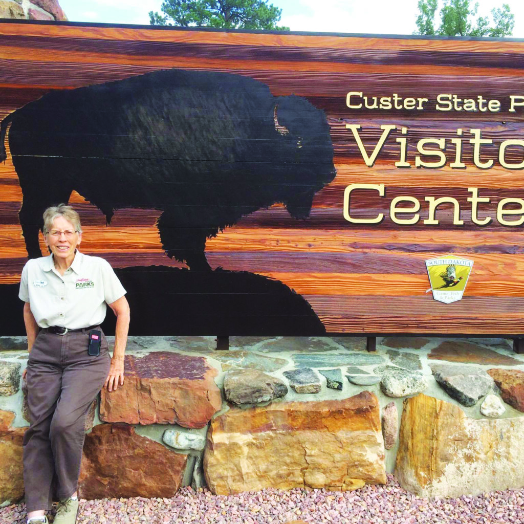 Solo female workamper stands in front of sign at Custer State Park visitor center