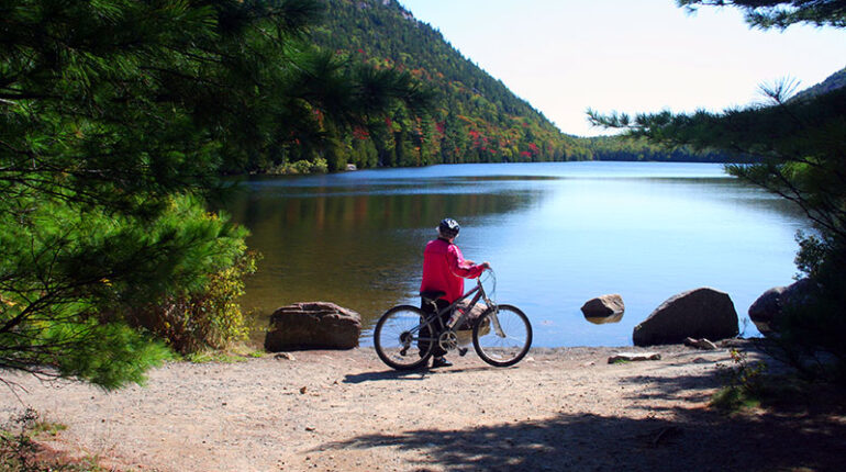 Woman standing with bike looking at lake on a carriage road in Acadia National Park